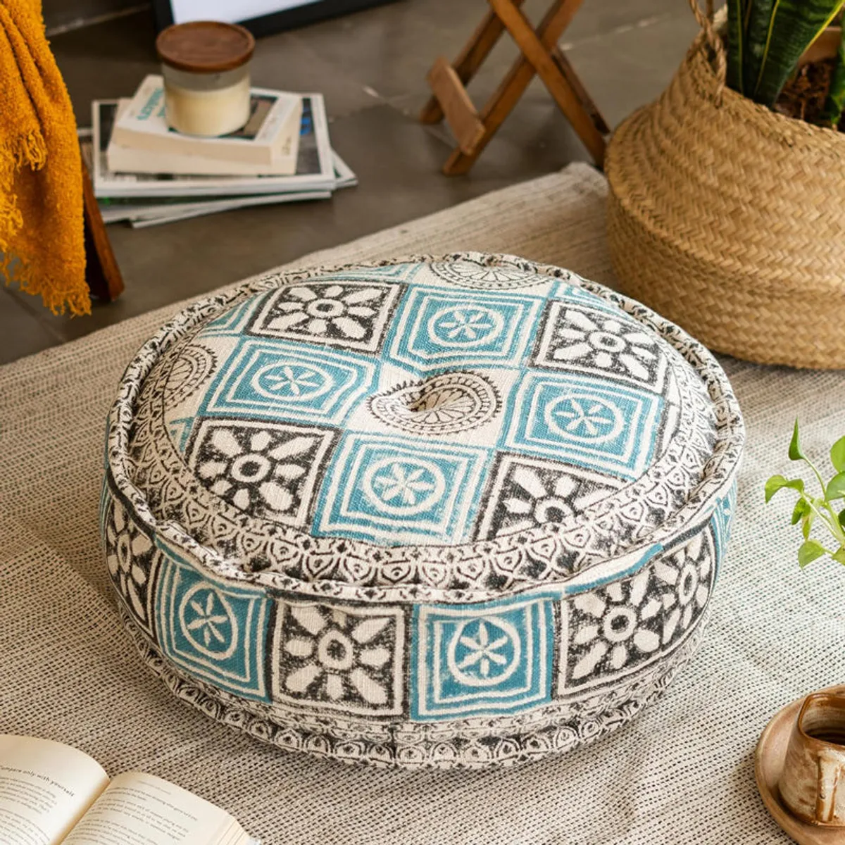 Round blue and cream patterned cushion styled with plants, books and a mustard throw.