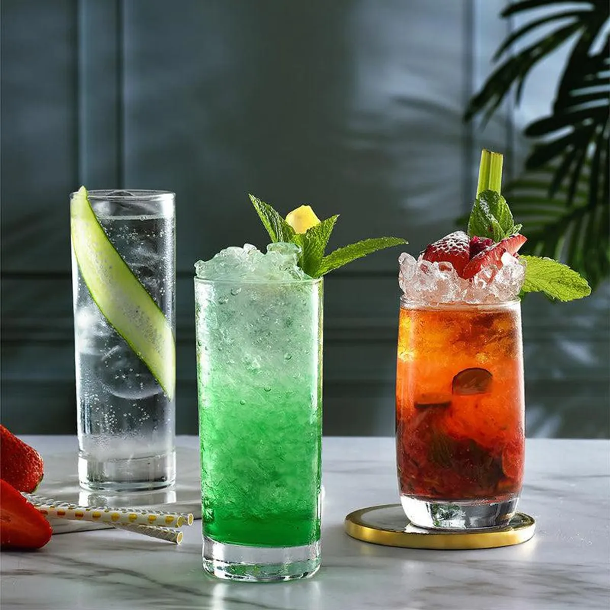 Three clear tumblers filled with colourful iced drinks and garnished with fruit and mint