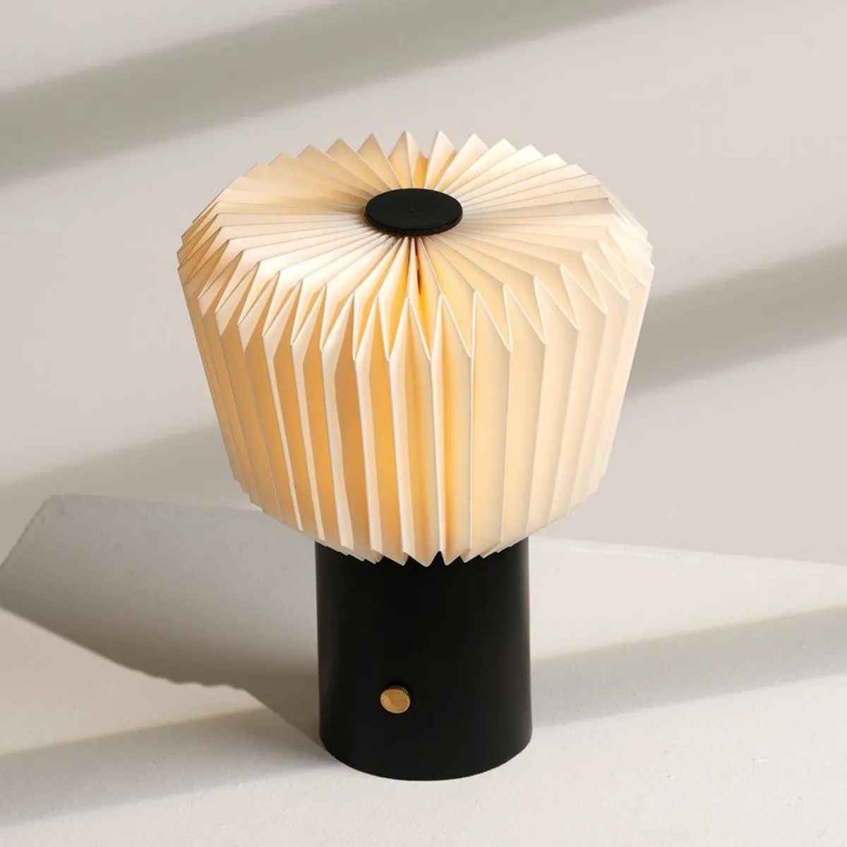 Off-white pleated table lamp with a black base shown in bright daylight