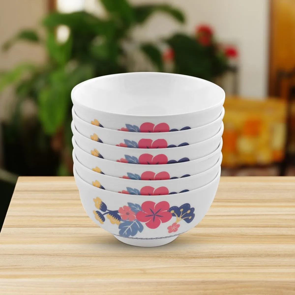 Stack of six white bowls with colourful floral designs on a wooden table