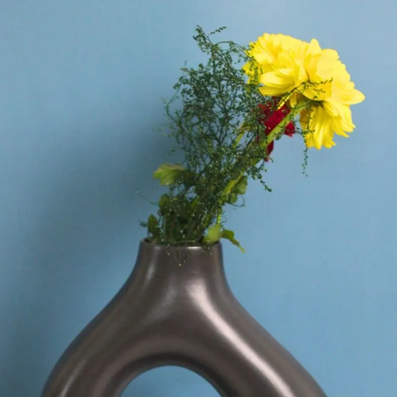 Close view of a black sculptural vase with yellow flowers against a blue background