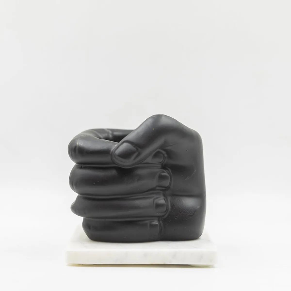 Side view of black fist-shaped pen stand on white marble base