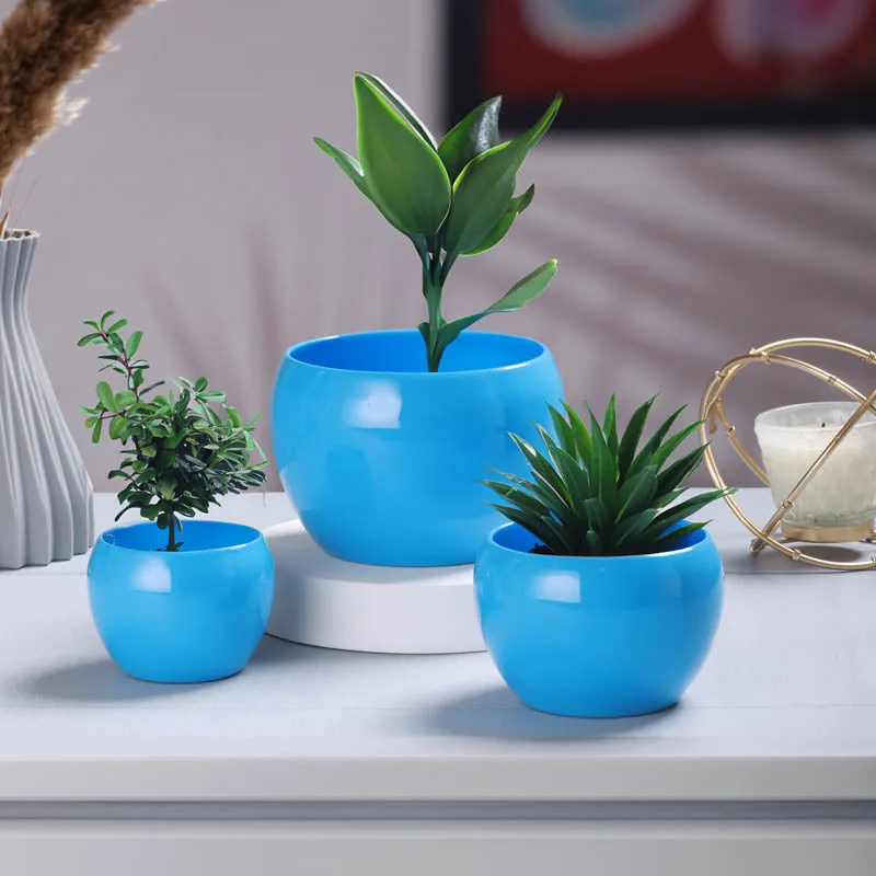 Three glossy blue round planters styled on a tabletop with decorative plants.