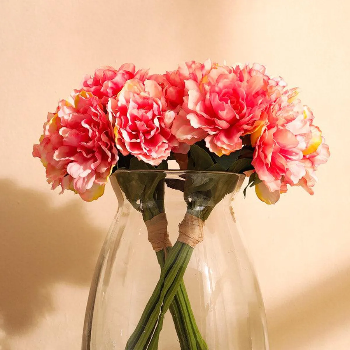 Pink artificial peony bouquet shown close up in a clear vase
