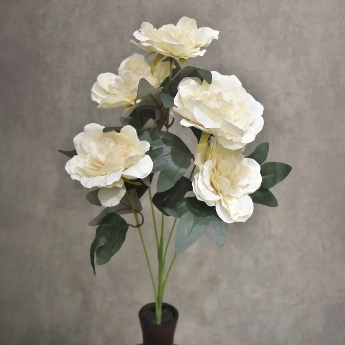 Close view of five off-white artificial peony blooms with green leaves