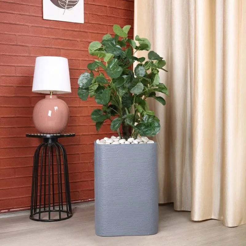 Grey planter with a leafy plant against a red brick wall