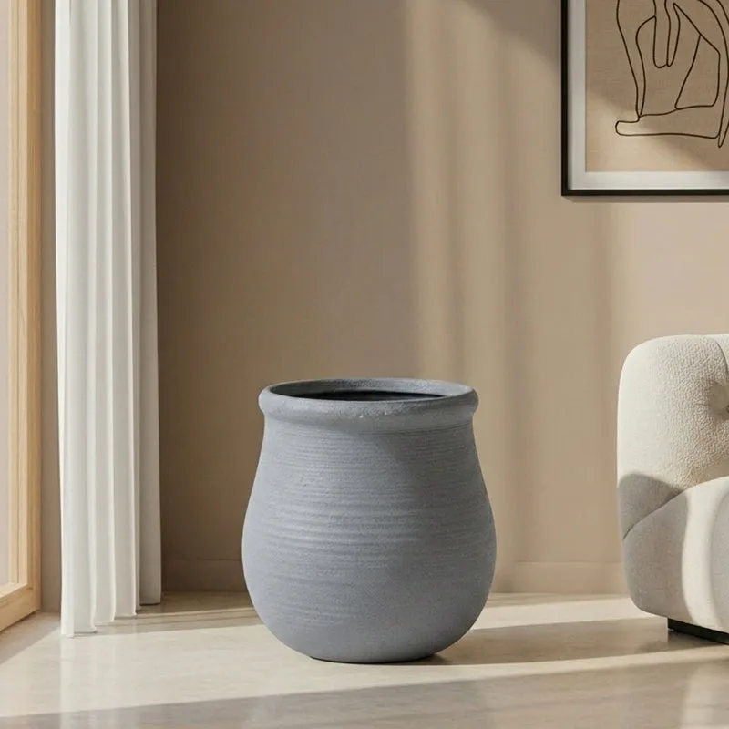 Empty grey rounded floor planter with a wide rim beside a neutral armchair