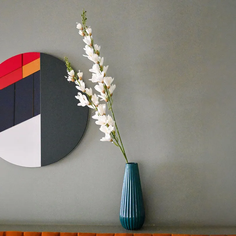 White artificial flower stick displayed in a tall teal vase against a grey wall