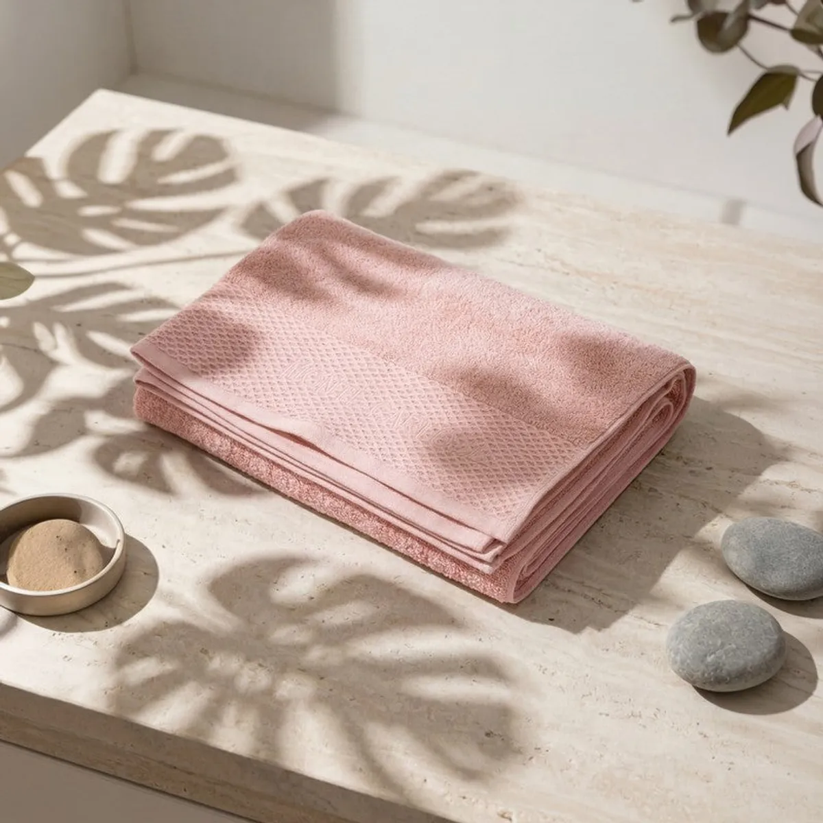 Folded light pink bath towel with textured border on a tabletop