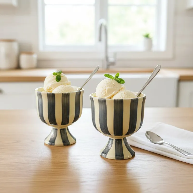 Two striped pedestal dessert cups with vanilla ice cream and spoons on a table