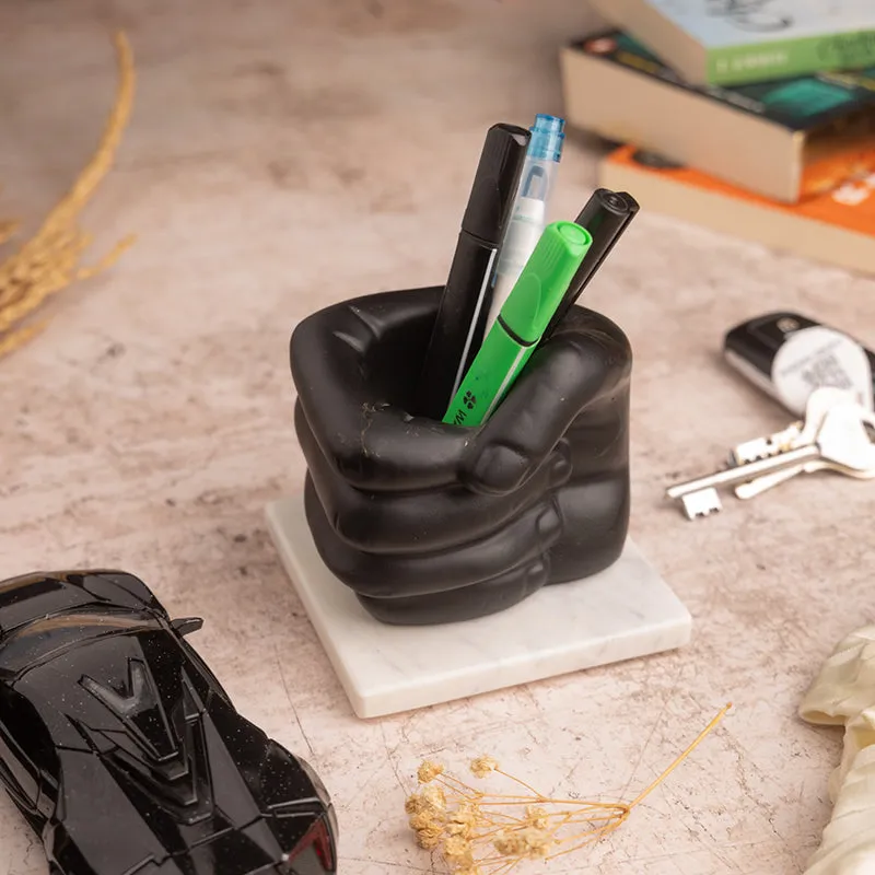 Angled view of black fist-shaped pen stand on white marble base