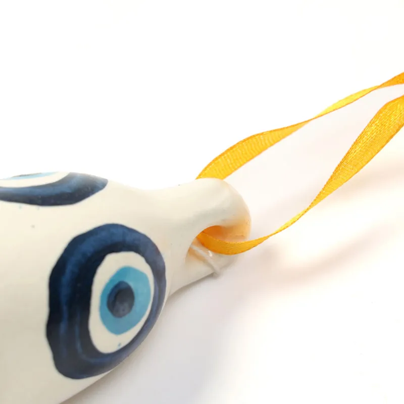 Close-up of white ceramic bell with blue evil eye motif and yellow hanging ribbon