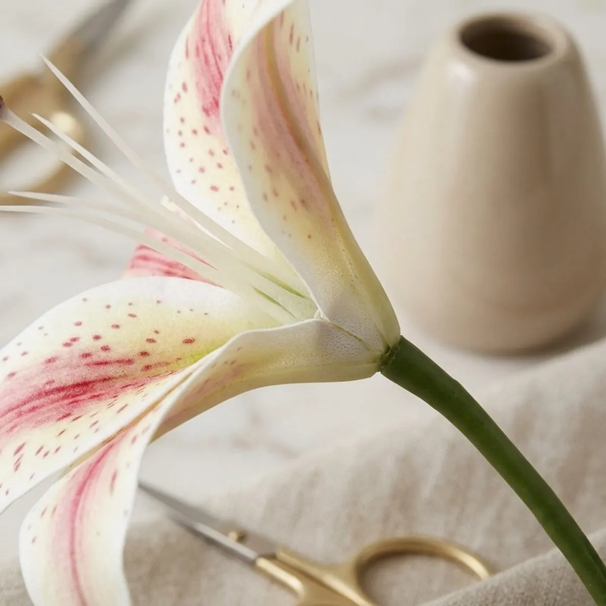 Close-up of a white and pink speckled artificial lily petal and green stem