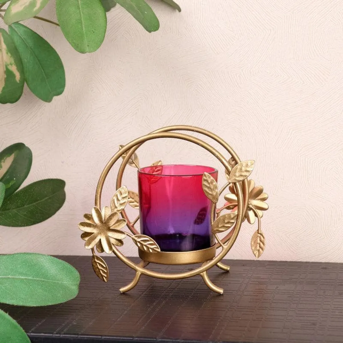 Gold floral tealight holder with red-purple glass cup on tabletop