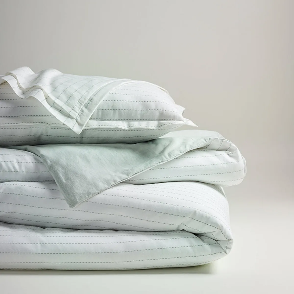 Folded white striped duvet cover and pillows in a minimal setting