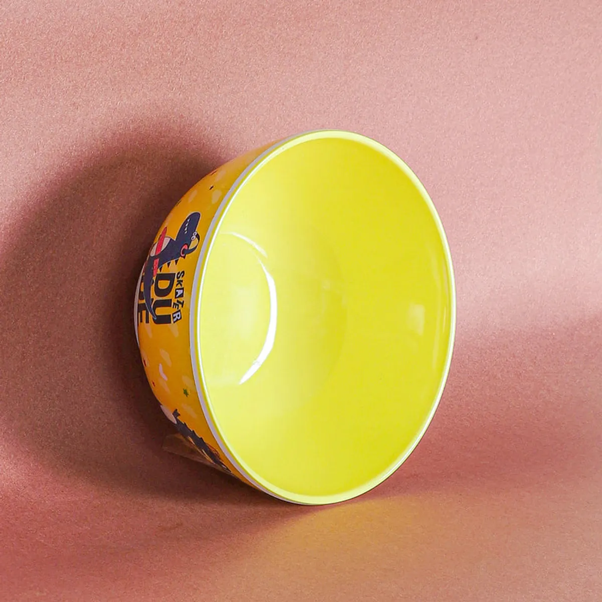 Yellow snack bowl lying on its side, showing its bright interior and dinosaur artwork.