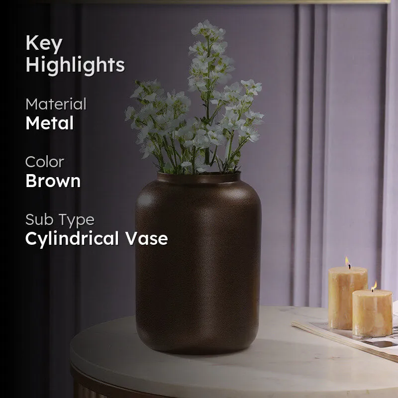 Brown metal vase with white flowers on a table beside candles