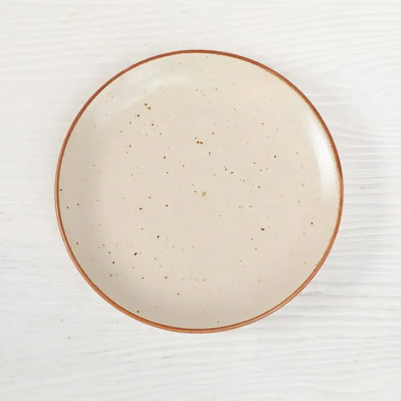 Close-up of a round cream ceramic plate with speckles and a brown edge