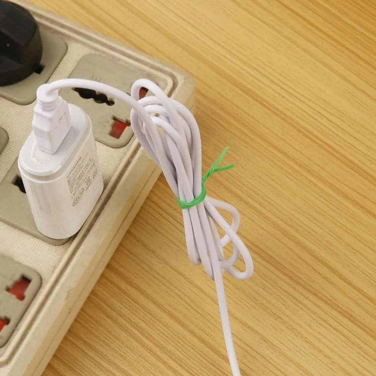 Green tie organising a white cable on a wooden desk