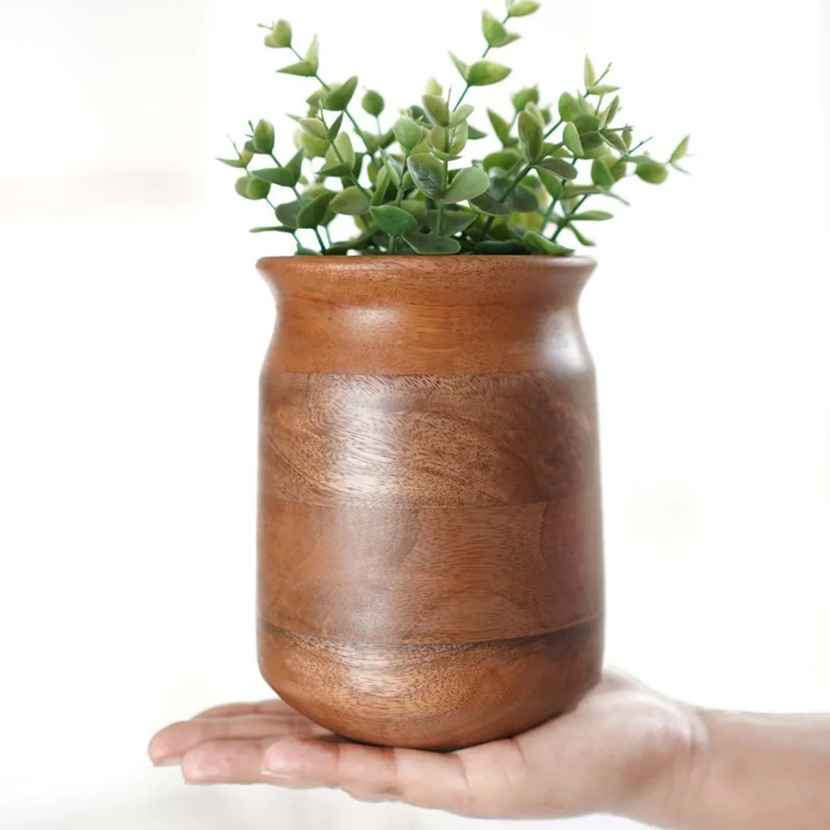 Dark brown wooden vase with green stems resting on an open palm