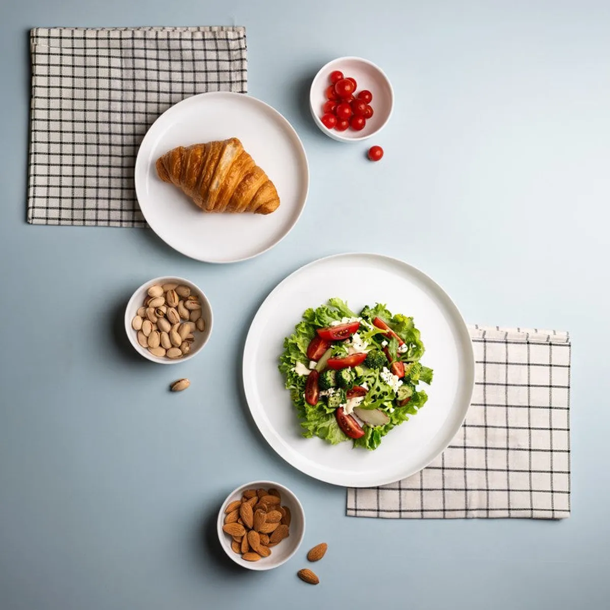 White dinnerware styled with salad, croissant, nuts and checked napkins