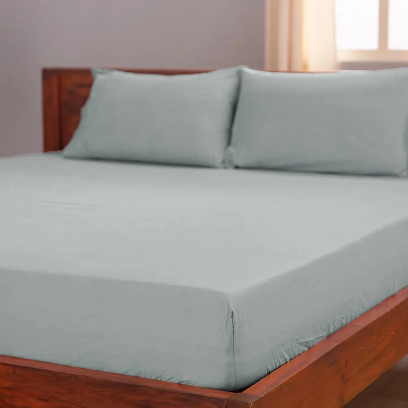 Light grey fitted bedsheet on a wooden bed with matching pillow covers