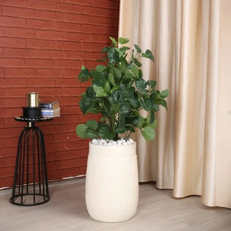White floor planter with a leafy plant beside a brick wall and curtains