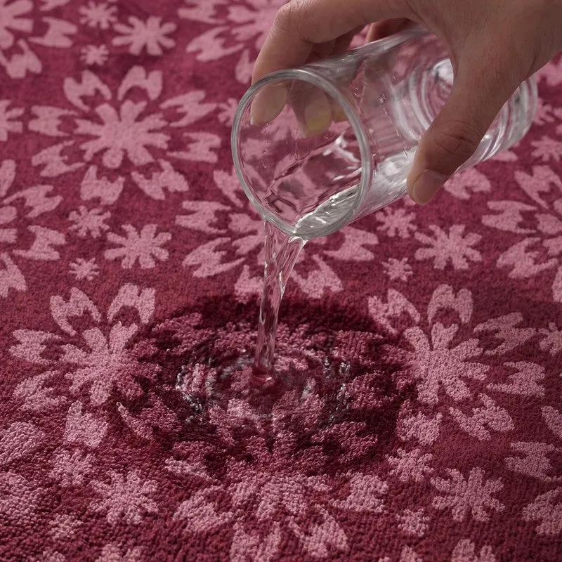 Close-up of water being poured onto the maroon floral towel surface.