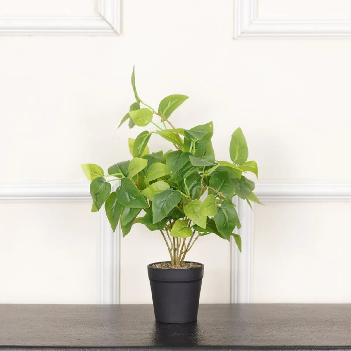 Green artificial leafy plant in a black pot on a dark tabletop