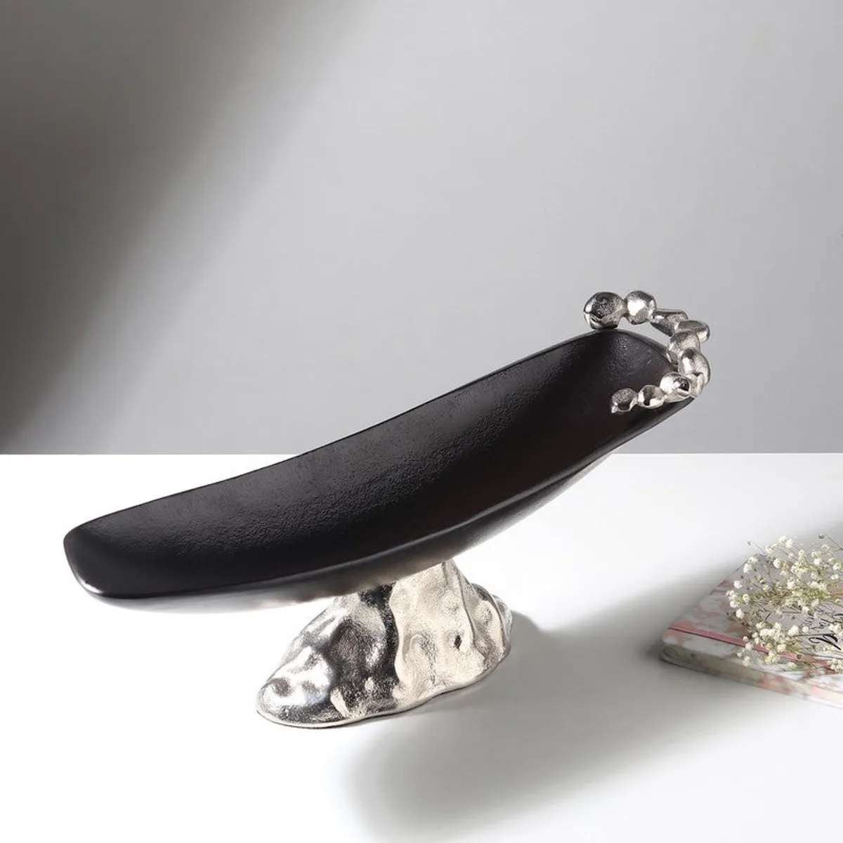 Side view of a long black fruit bowl with a silver sculptural base