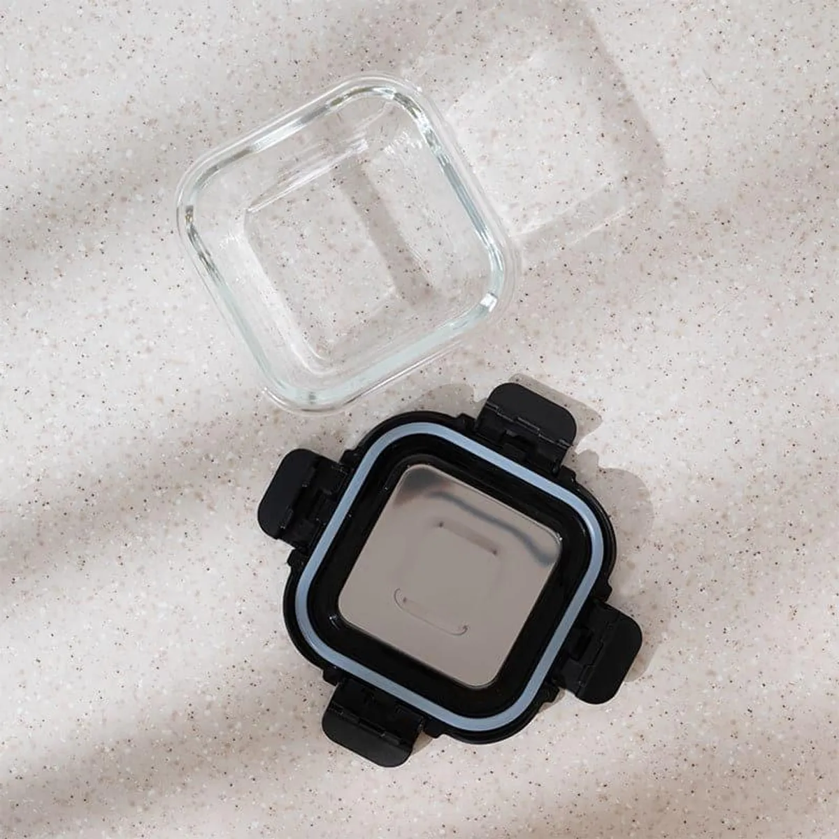 Top view of the clear square glass base and black lid components