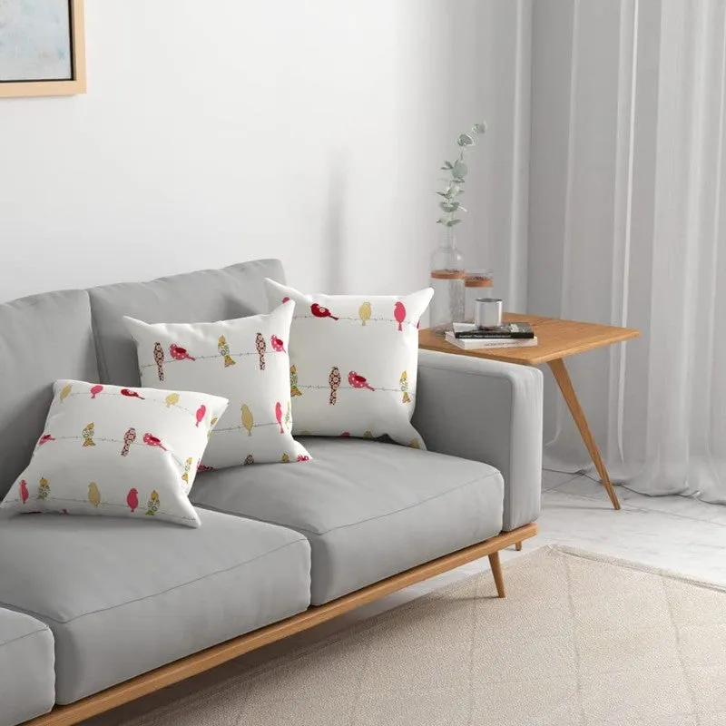 Three bird-print cushion covers styled on a light grey sofa beside a wooden side table