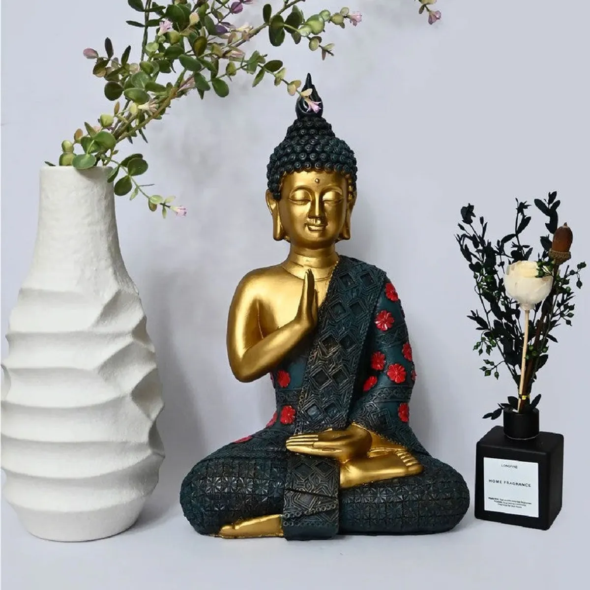 Buddha idol with gold finish, teal robe and red floral accents beside decor pieces