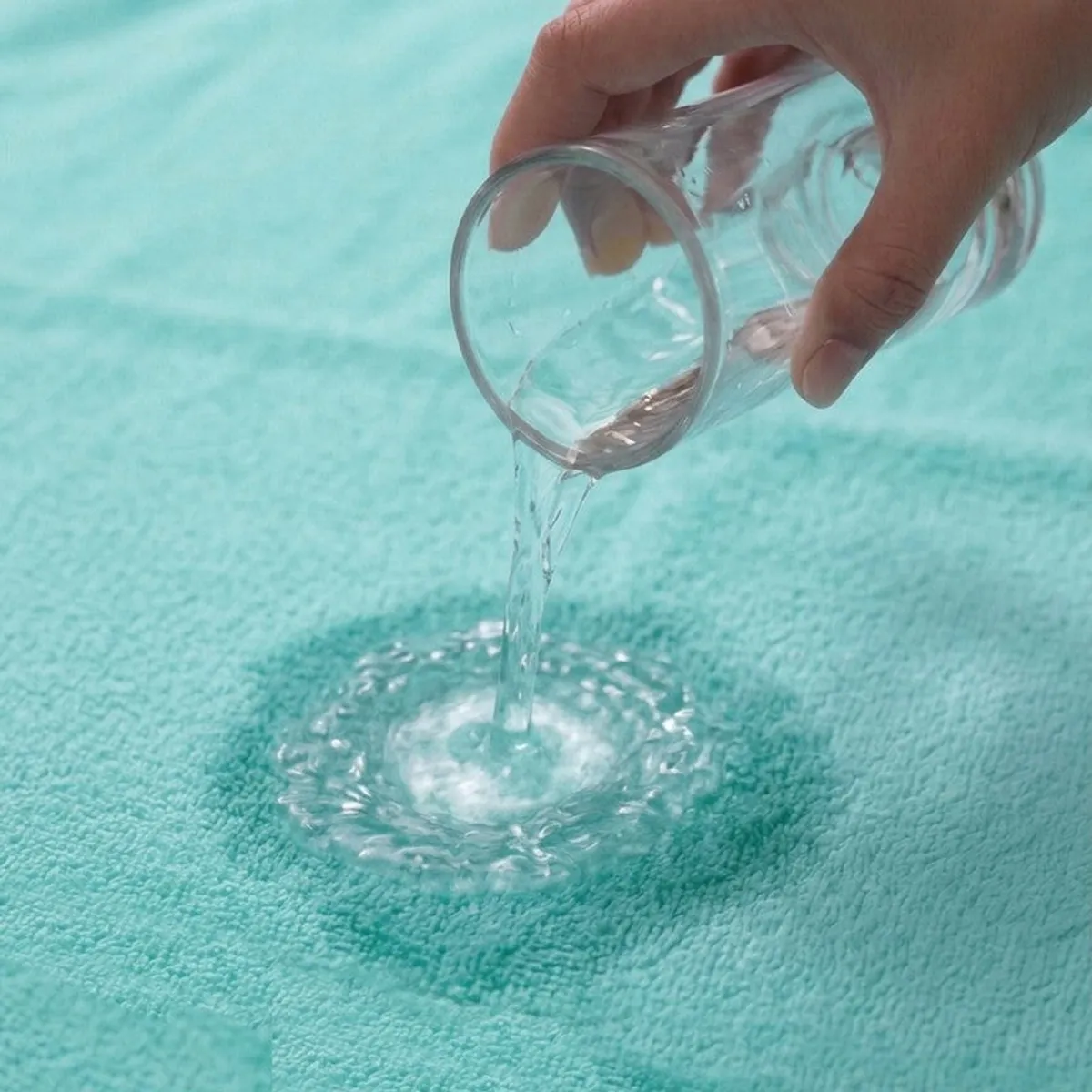 Water being poured onto the absorbent surface of a turquoise towel