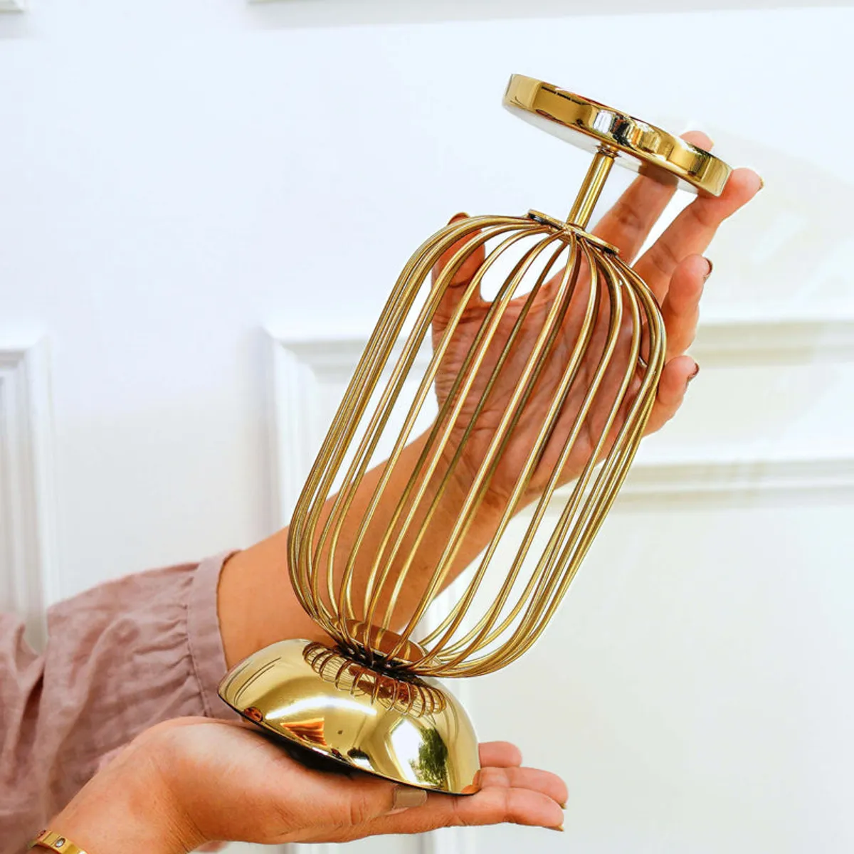 Gold candle holder shown being held to display its open cage shape