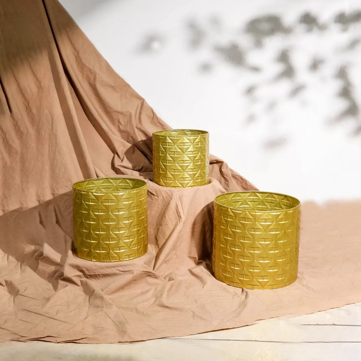 Three gold textured cylindrical planters arranged at different heights on a draped fabric backdrop.