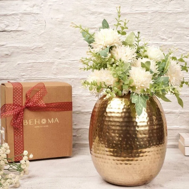 Gold hammered oval vase with white flowers beside a gift box