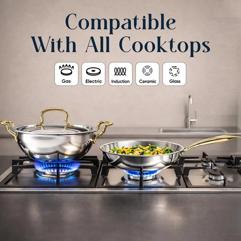 Silver kadhai and frying pan with gold handles on a gas cooktop