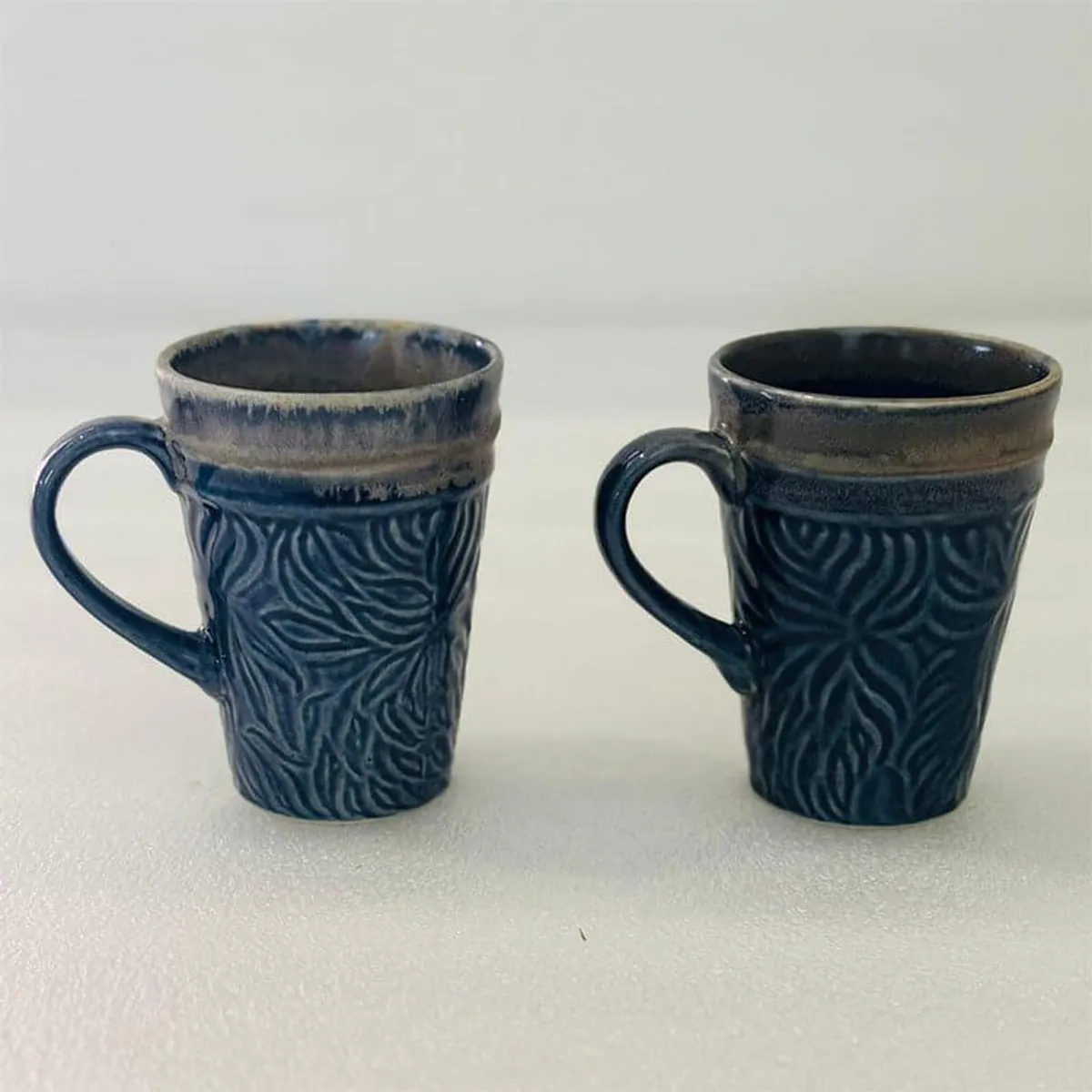 Two dark blue ceramic mugs with leafy textured bodies and glossy contrasting rims