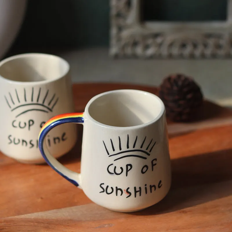White sunshine ceramic mug with colourful handle, shown with another mug in the background