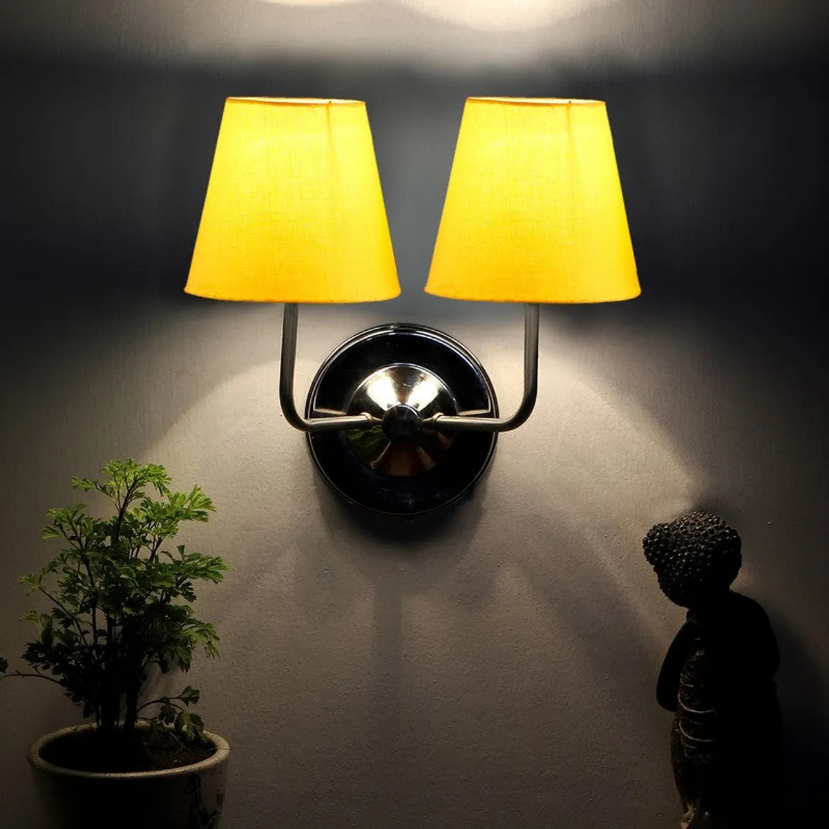 Lit wall lamp with yellow shades and steel base against a dark wall
