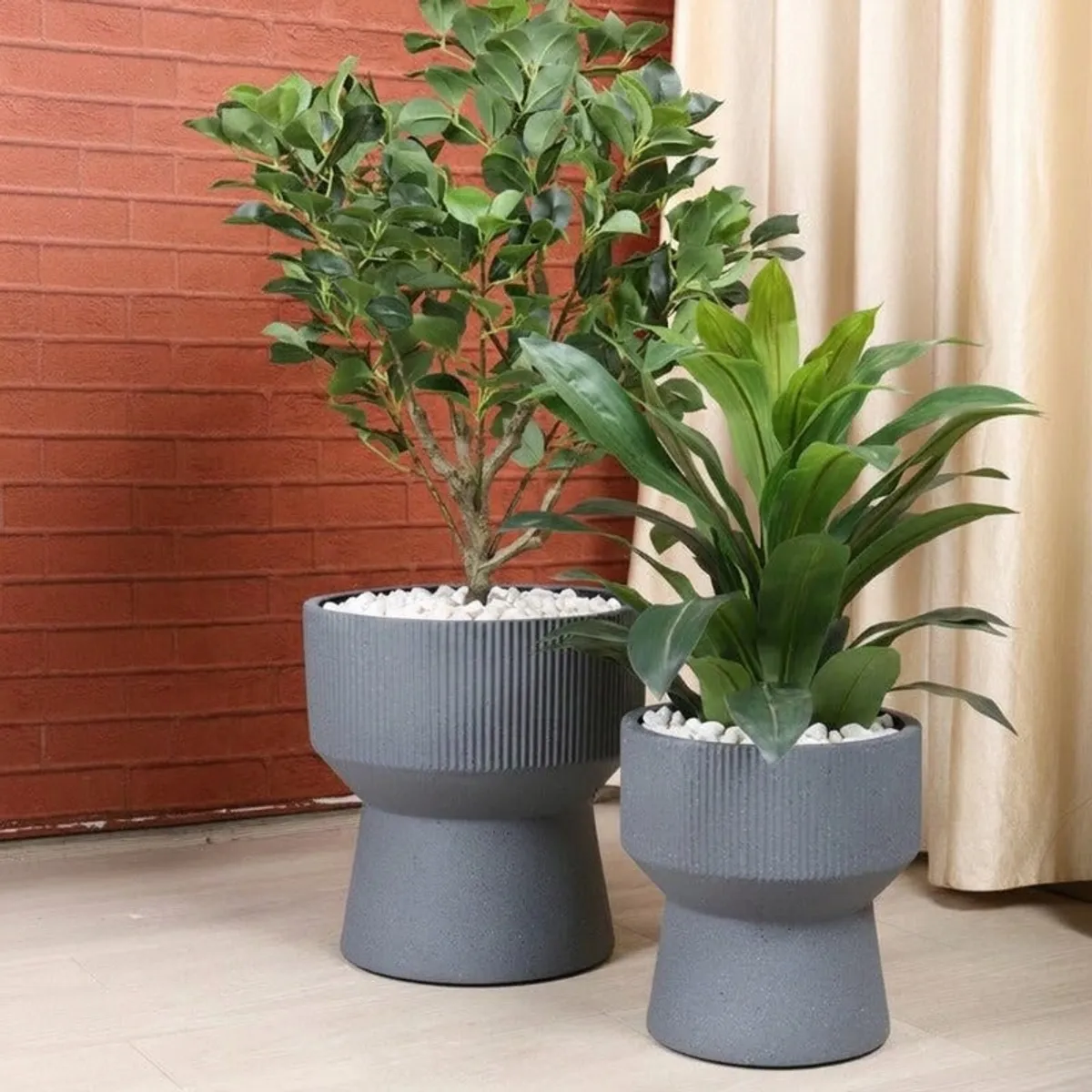 Grey hourglass planter with ribbed upper section displayed with green plants indoors