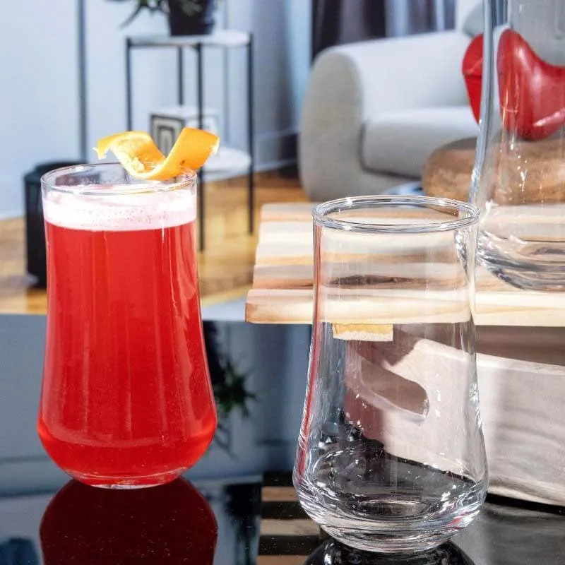 One empty clear tumbler beside a filled red drink glass