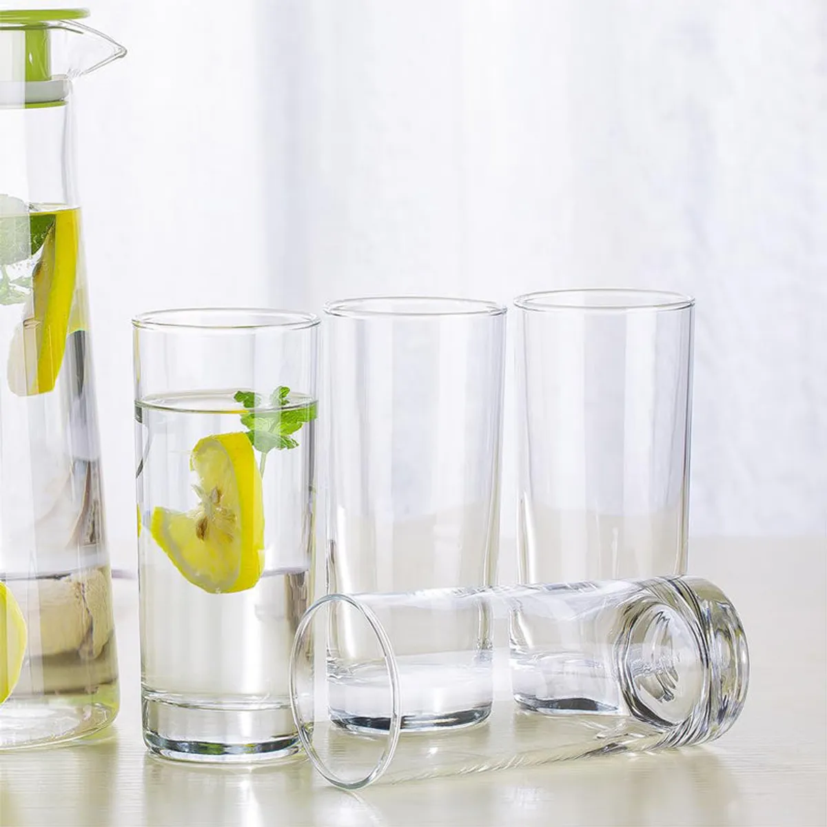 Clear tumblers with water and fruit beside a glass pitcher on a table