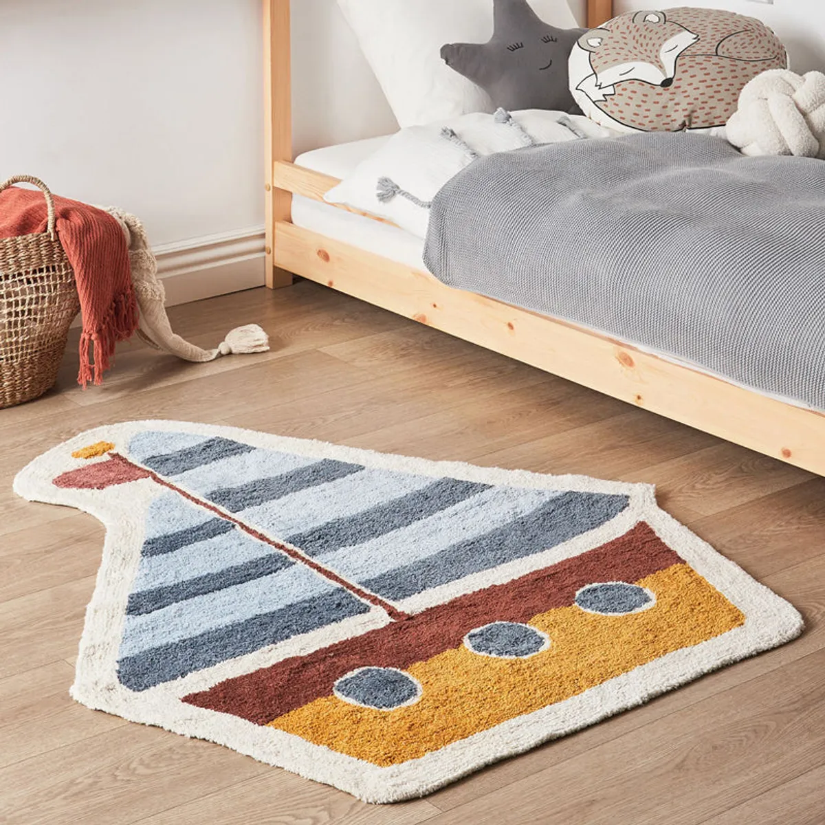 Sailboat-shaped plush rug with blue striped sail and yellow and rust boat details on a bedroom floor.