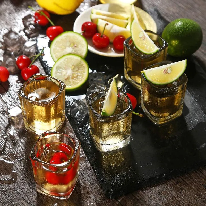 Five transparent square shot glasses with drinks, garnished with lime and cherries