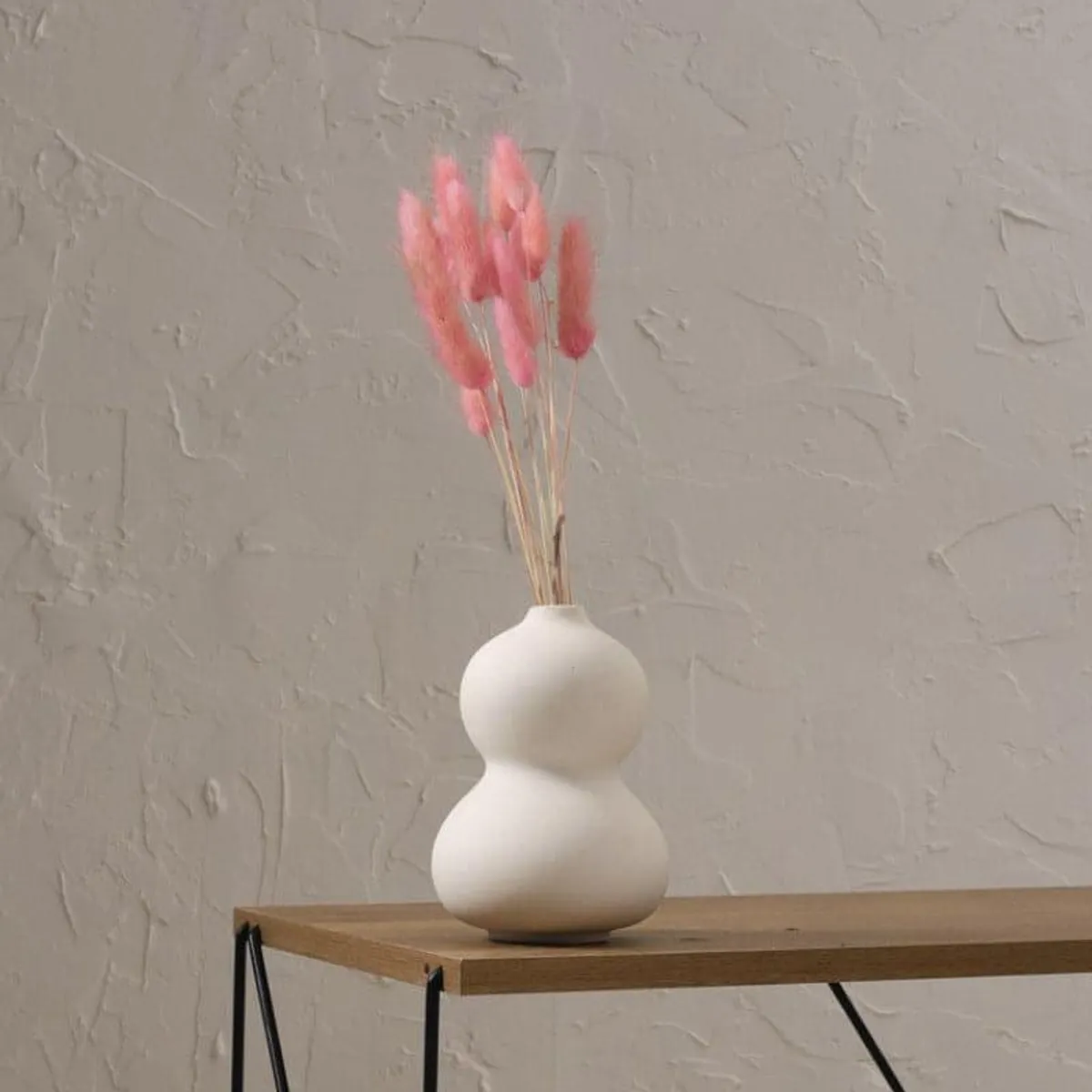 White bubble vase with pink dried stems on a wooden table
