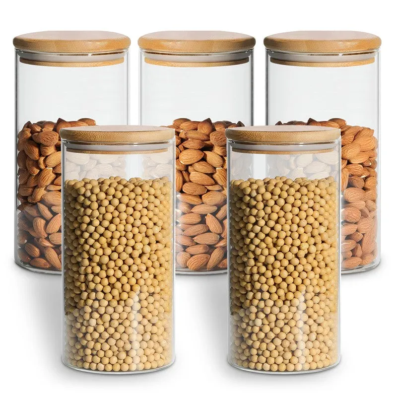 Five transparent glass jars with natural-toned lids, filled with nuts and pulses.