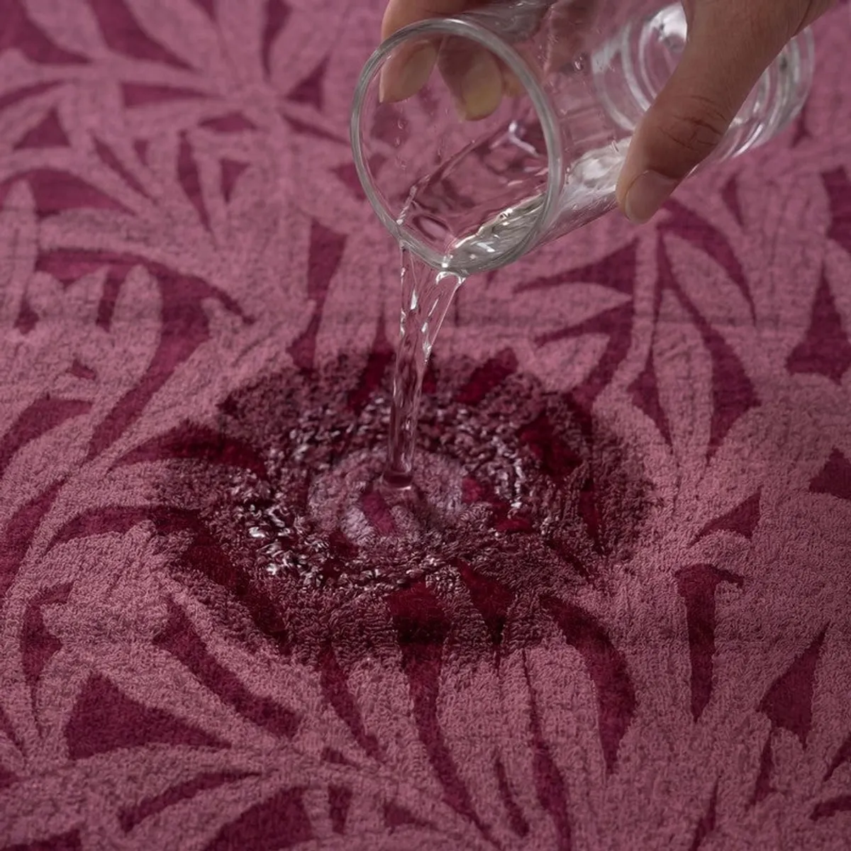 Water being poured onto the textured maroon floral towel surface.