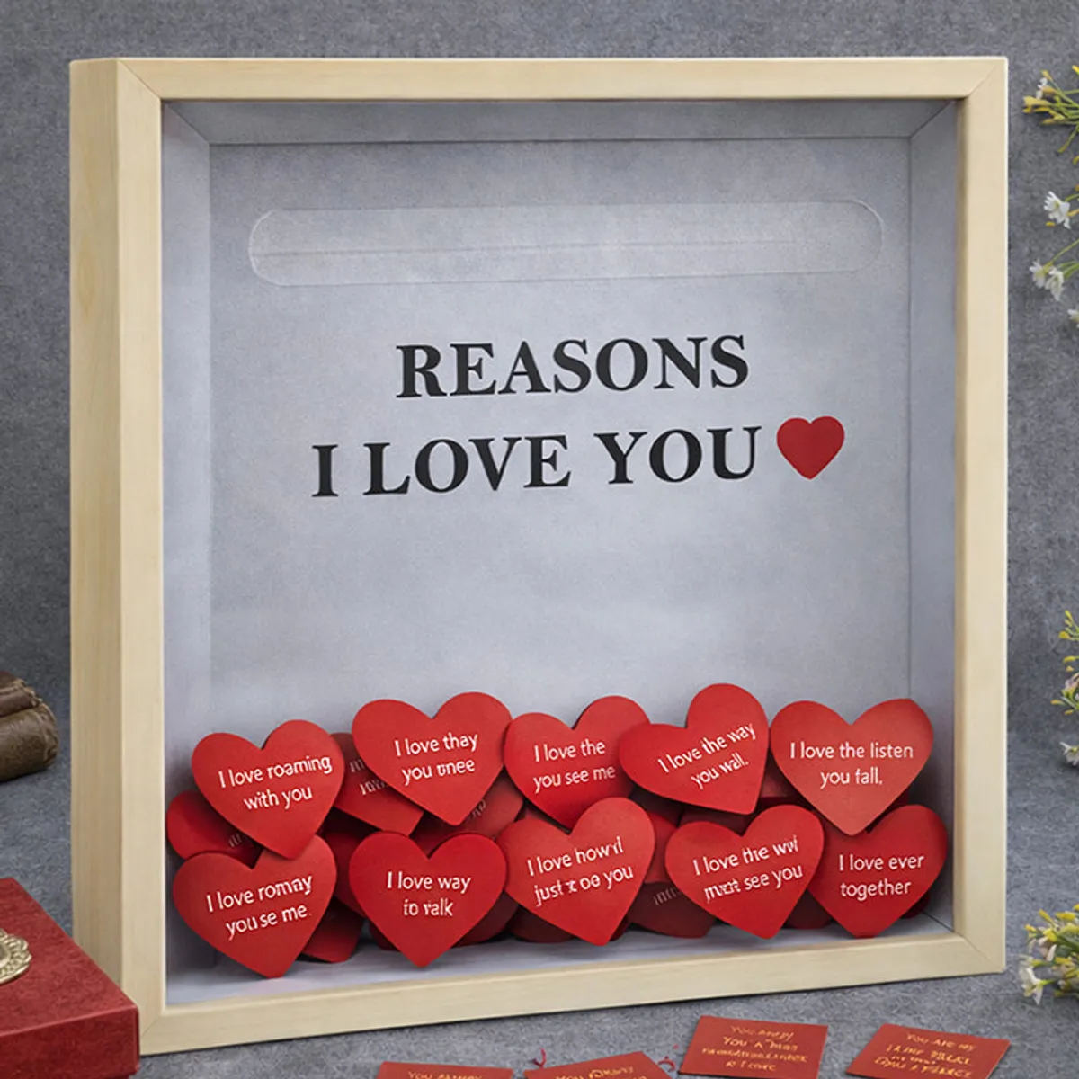 Square beige shadow box filled with red heart-shaped love notes